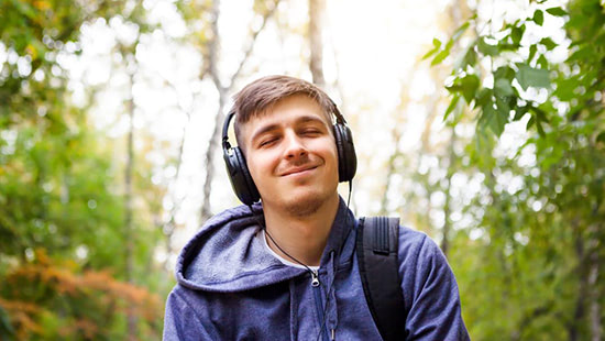 person in a forest smiling with headphones on