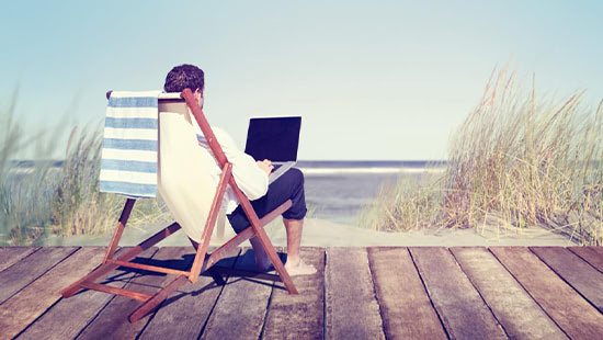 person sitting on a deck chair with a laptop on the beach